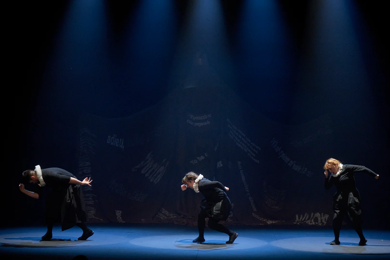 Tres actores de Guayominí Producciones interpretando la obra Hamlet en un escenario con iluminación teatral cenital y fondo oscuro.